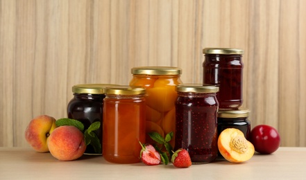 Photo of Jars of pickled fruits and jams on wooden table