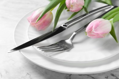 Stylish table setting with cutlery and tulips on white marble background, closeup