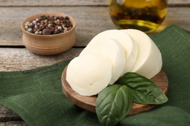 Photo of Board with tasty mozzarella slices and basil leaves on wooden table