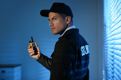 Professional security guard with portable radio set near window in dark room