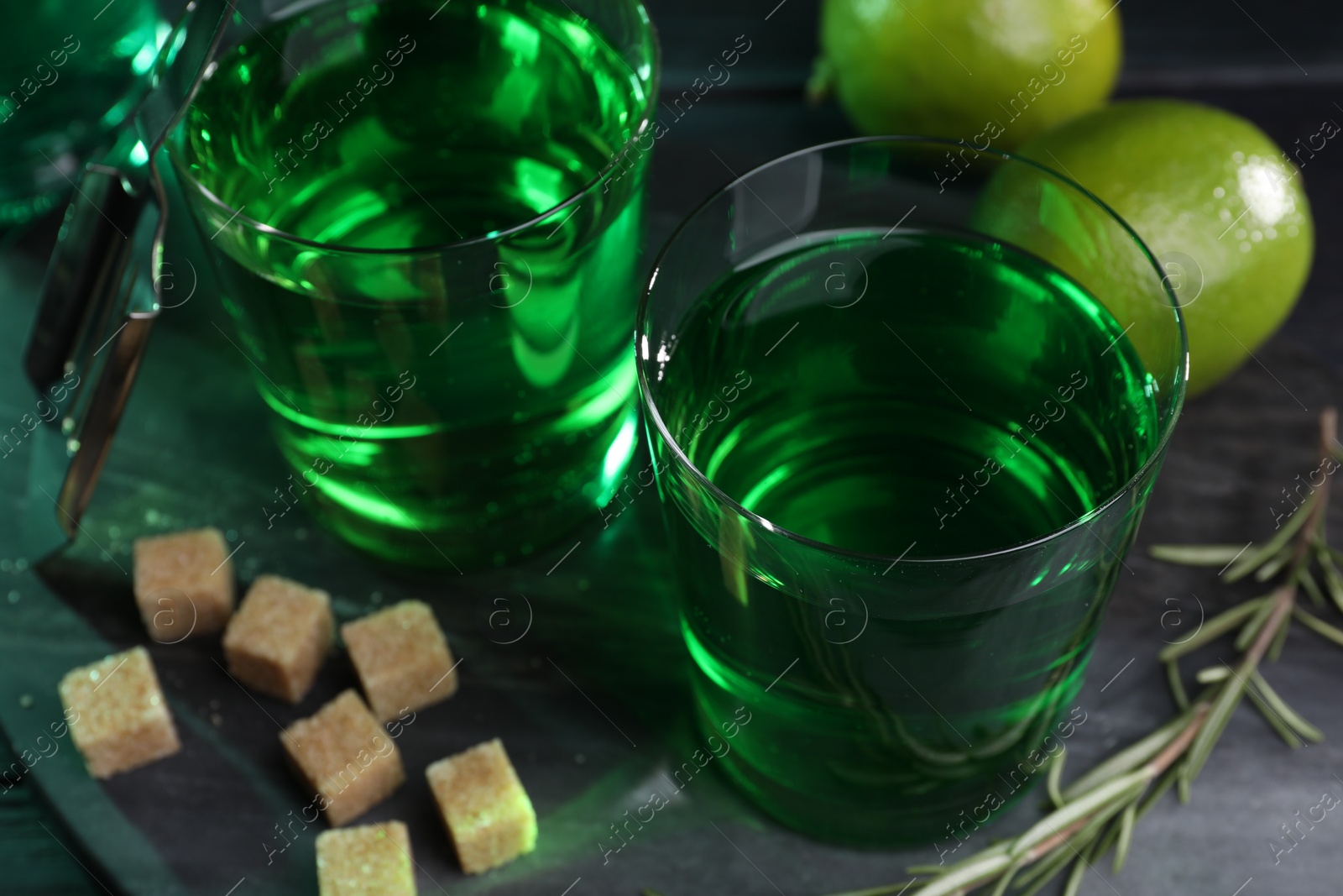 Photo of Absinthe in glasses, rosemary, brown sugar and lime on table, closeup. Alcoholic drink