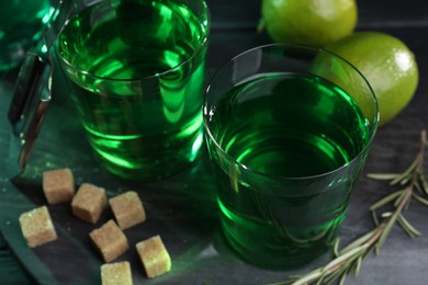 Photo of Absinthe in glasses, rosemary, brown sugar and lime on table, closeup. Alcoholic drink