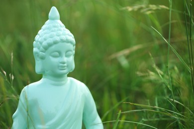 Photo of Decorative Buddha statue in green grass outdoors, closeup. Space for text