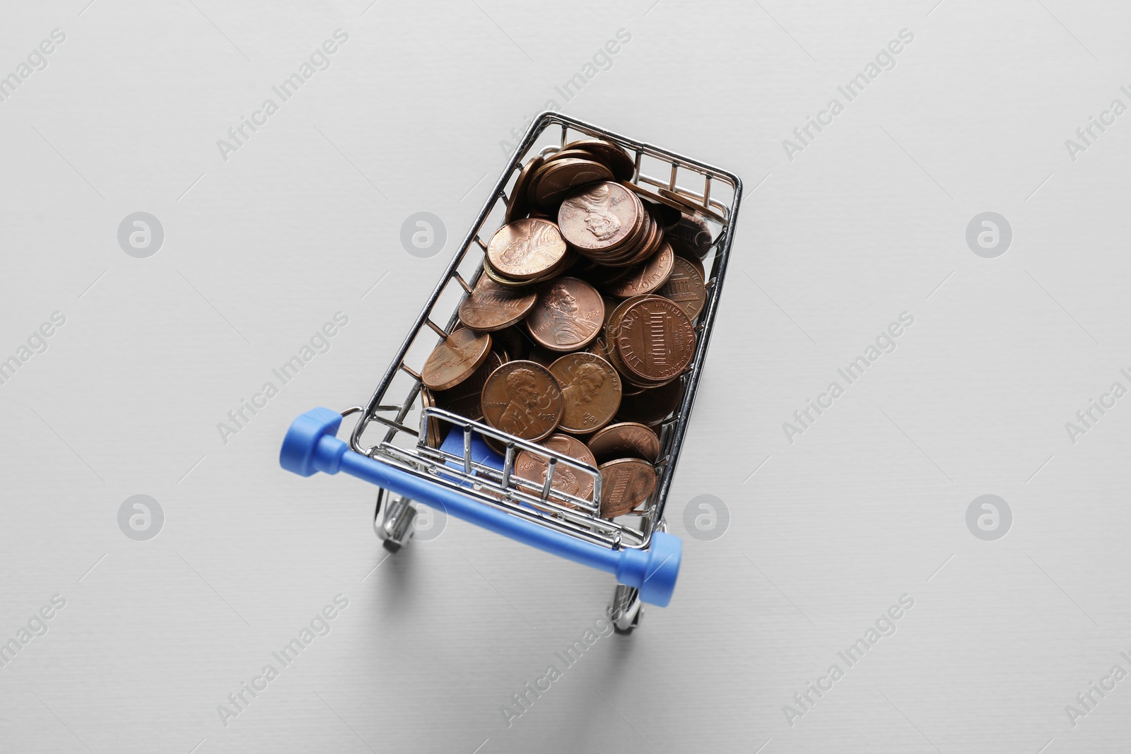 Photo of Small metal shopping cart with coins on light background, top view