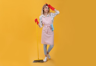 Photo of Young housewife with broom on yellow background