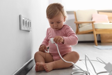 Photo of Cute baby playing with plug at home. Dangerous situation