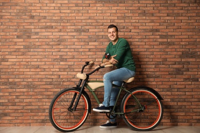 Photo of Portrait of handsome young man with bicycle near brick wall