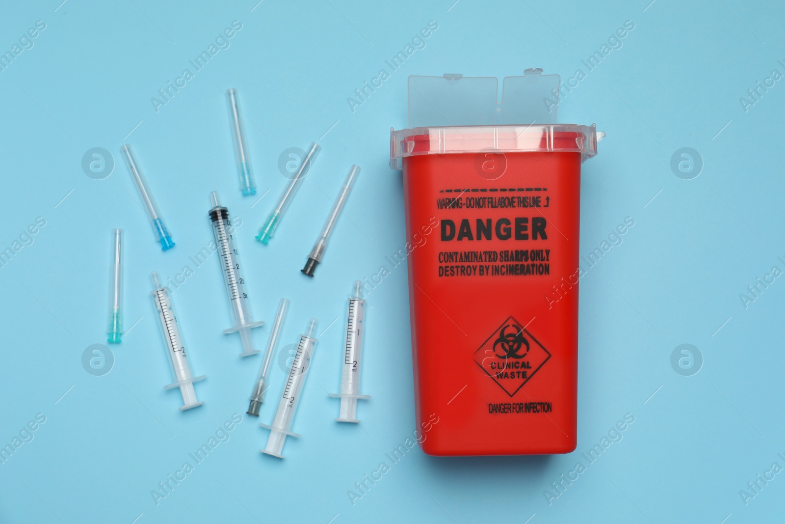 Photo of Disposable syringes, needles and sharps container on light blue background, flat lay