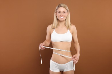 Photo of Slim woman measuring waist with tape on brown background. Weight loss