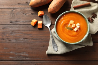 Flat lay composition with bowl of tasty sweet potato soup and space for text on wooden background