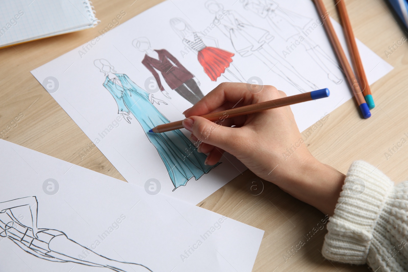 Photo of Fashion designer creating new clothes in sketchbook at wooden table, closeup