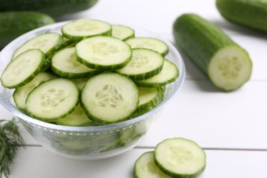 Photo of Cut cucumber in glass bowl and fresh vegetables on white wooden table, closeup