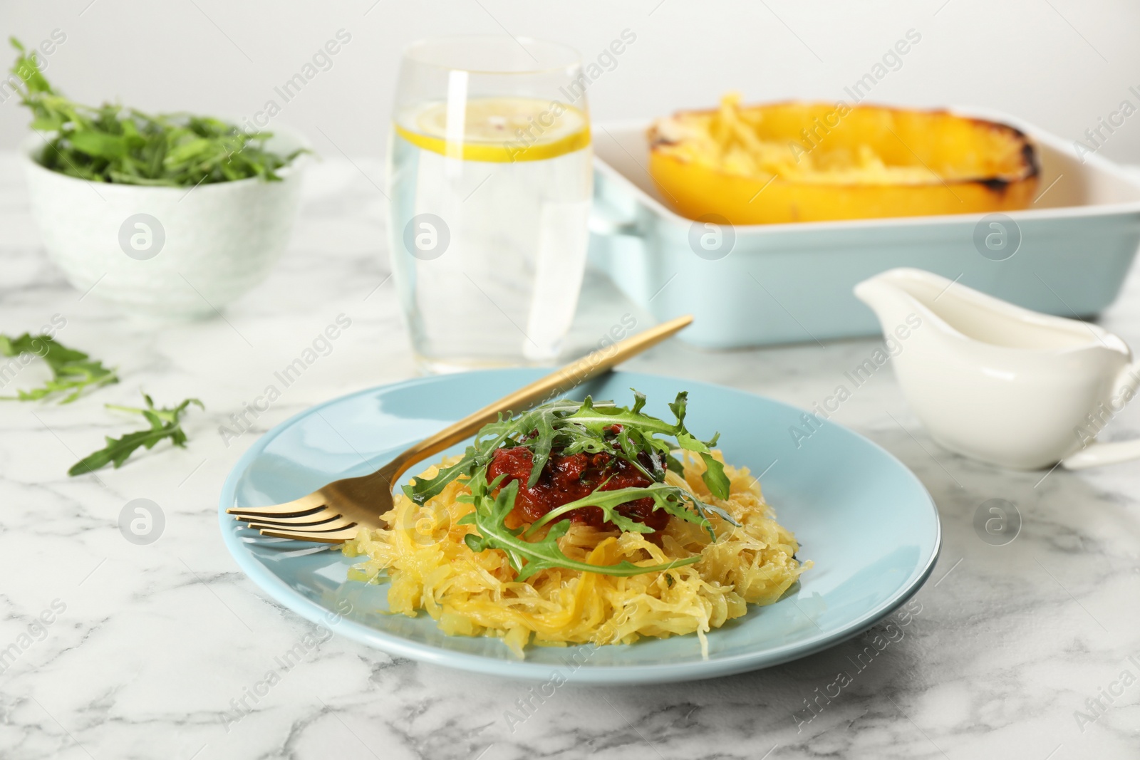 Photo of Tasty spaghetti squash with tomato sauce and arugula served on white marble table