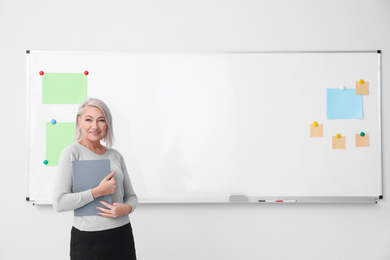 Mature teacher with notebook near whiteboard in classroom. Space for text