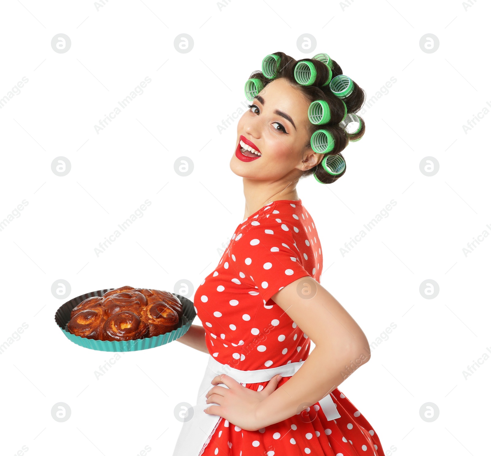 Photo of Funny young housewife with hair rollers holding homemade pastry on white background