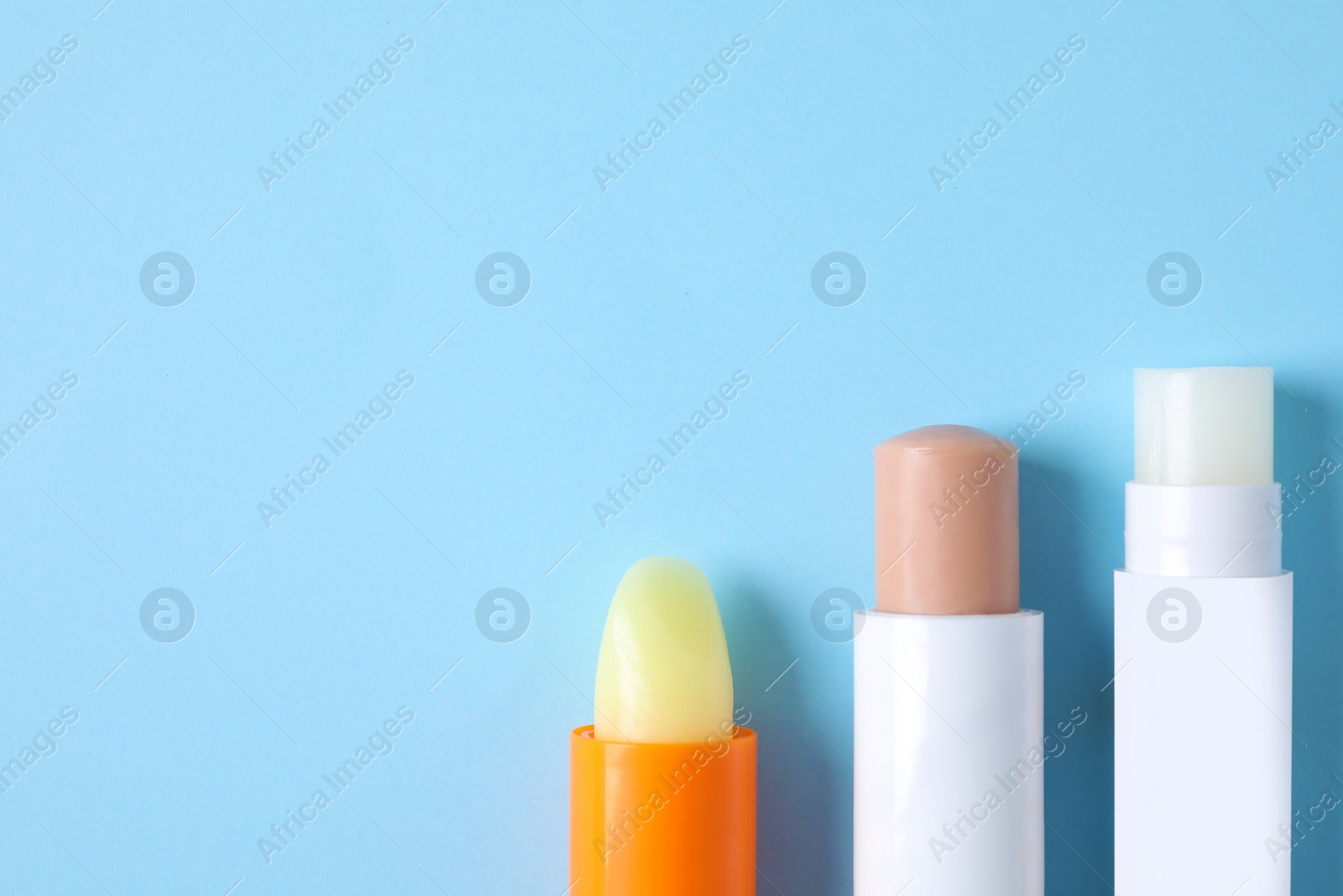 Photo of Hygienic lipsticks on light blue background, flat lay. Space for text