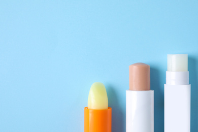 Photo of Hygienic lipsticks on light blue background, flat lay. Space for text