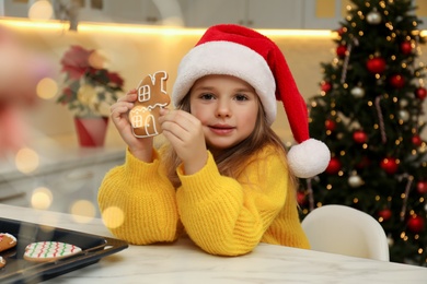 Photo of Cute little girl with freshly baked Christmas gingerbread cookie at table indoors