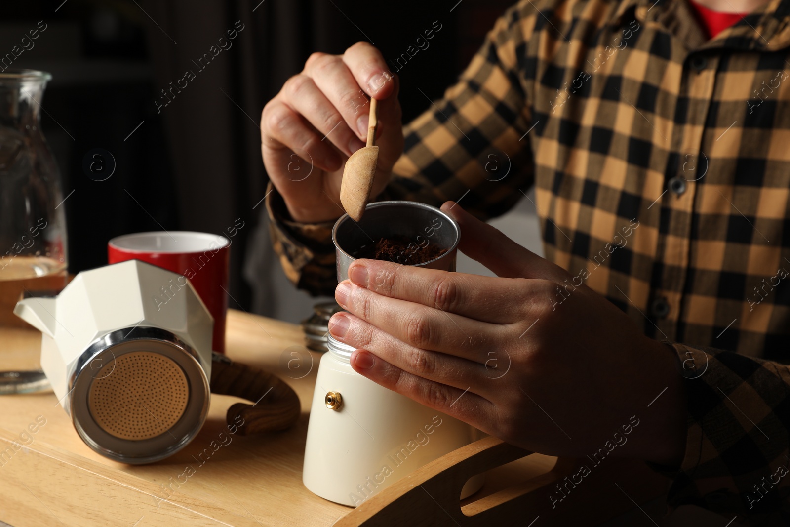 Photo of Man putting ground coffee into moka pot at table indoors, closeup