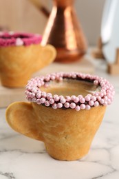 Photo of Delicious edible biscuit cup of coffee decorated with sprinkles on white marble table