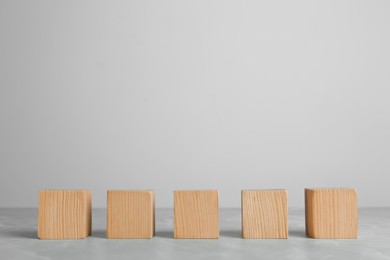 Photo of Row of blank wooden cubes on grey table against light background. Space for text