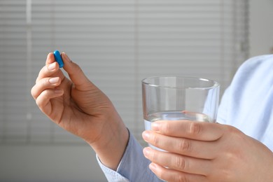 Woman with pill and glass of water on blurred background, closeup