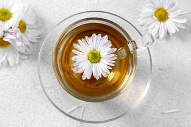 Glass cup of delicious chamomile tea on white table, top view