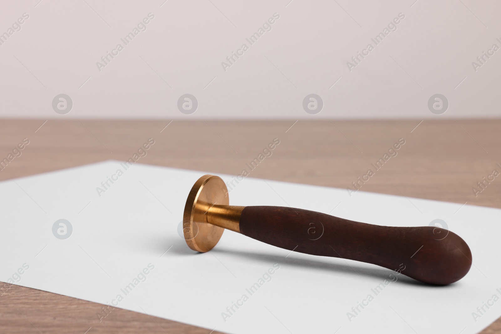 Photo of One stamp tool and sheet of paper on wooden table, closeup