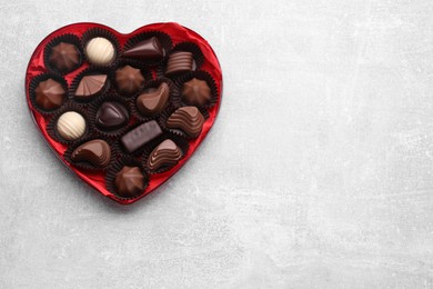 Photo of Heart shaped box with delicious chocolate candies on light grey table, top view. Space for text