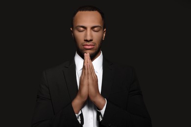 African American man with clasped hands praying to God on black background