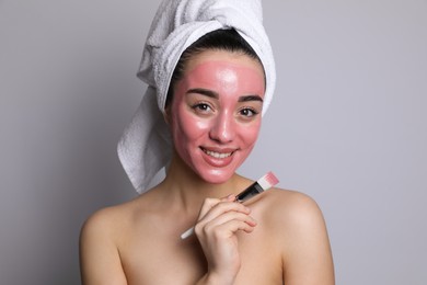 Photo of Woman applying pomegranate face mask on grey background