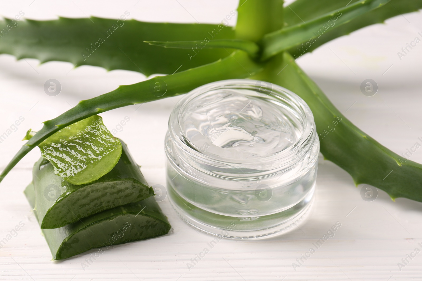 Photo of Jar of cosmetic gel and cut aloe vera leaves on white wooden table, closeup