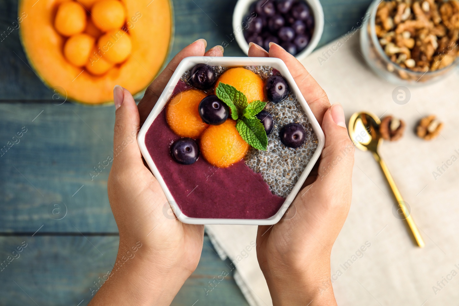 Photo of Woman holding bowl of tasty acai smoothie over wooden table