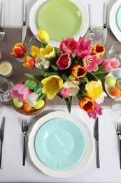 Photo of Easter celebration. Festive table setting with beautiful flowers and painted eggs, flat lay