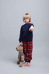 Photo of Boy in pajamas with toy bear sleepwalking on light gray background
