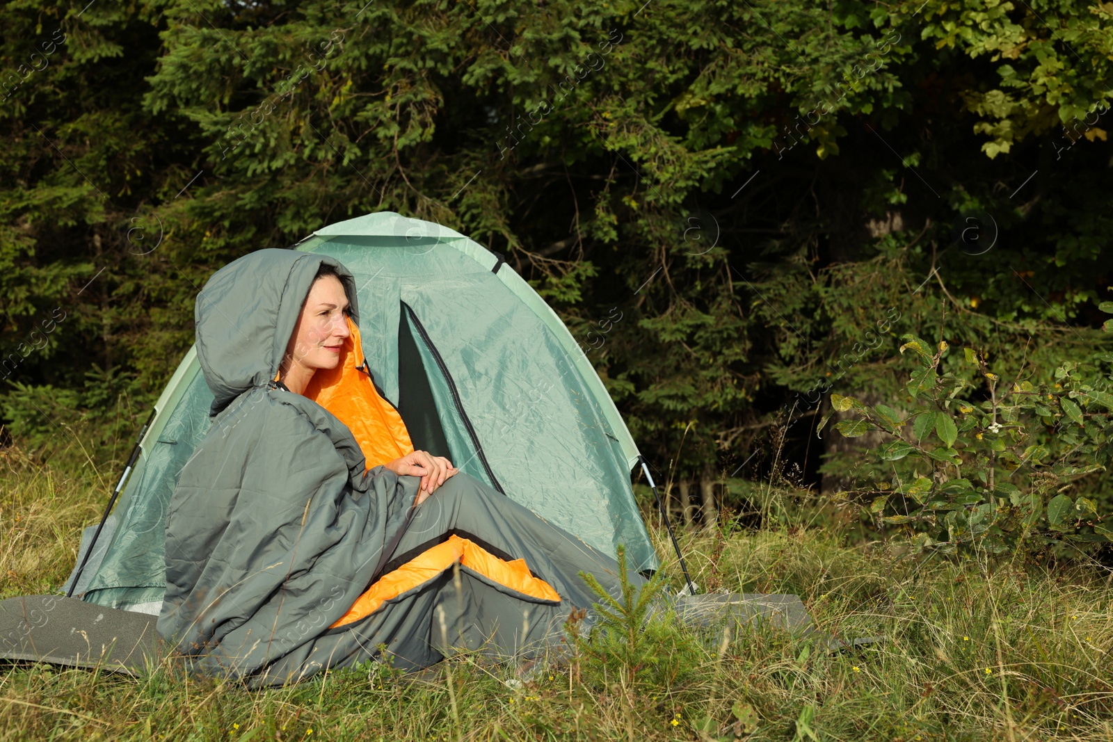 Photo of Mature woman in sleeping bag near camping tent outdoors