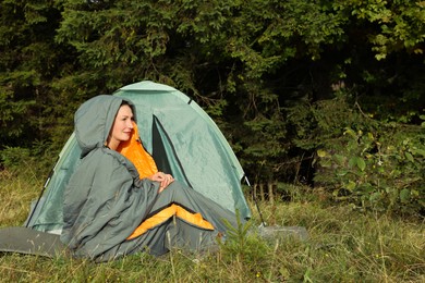 Photo of Mature woman in sleeping bag near camping tent outdoors