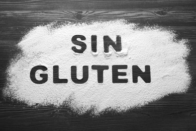 Photo of Words Sin gluten written with flour on dark wooden table, top view
