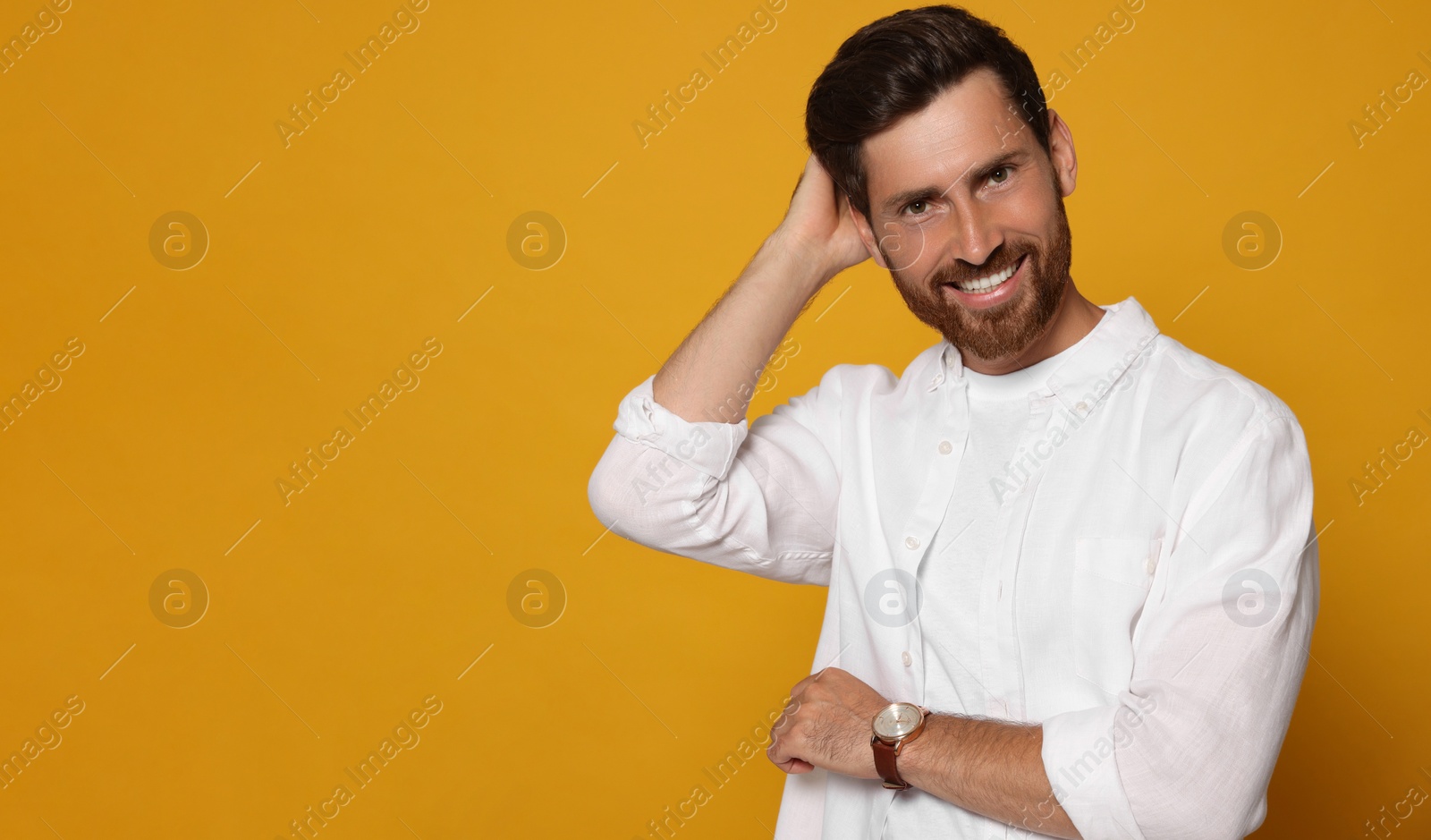 Photo of Portrait of smiling bearded man with wristwatch on orange background. Space for text