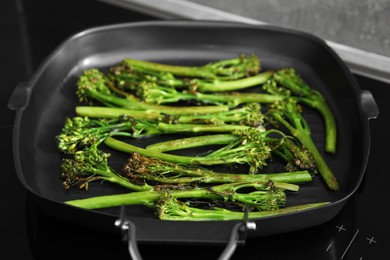 Photo of Grill pan with tasty cooked broccolini on cooktop, closeup