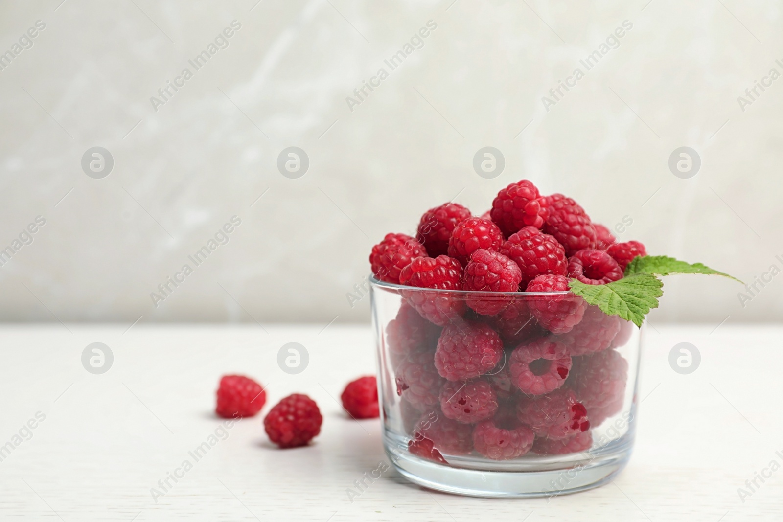 Photo of Glass with ripe aromatic raspberries on table