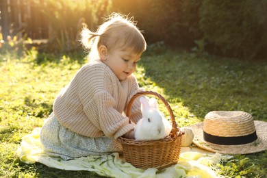 Photo of Cute little girl with adorable rabbit on green grass outdoors
