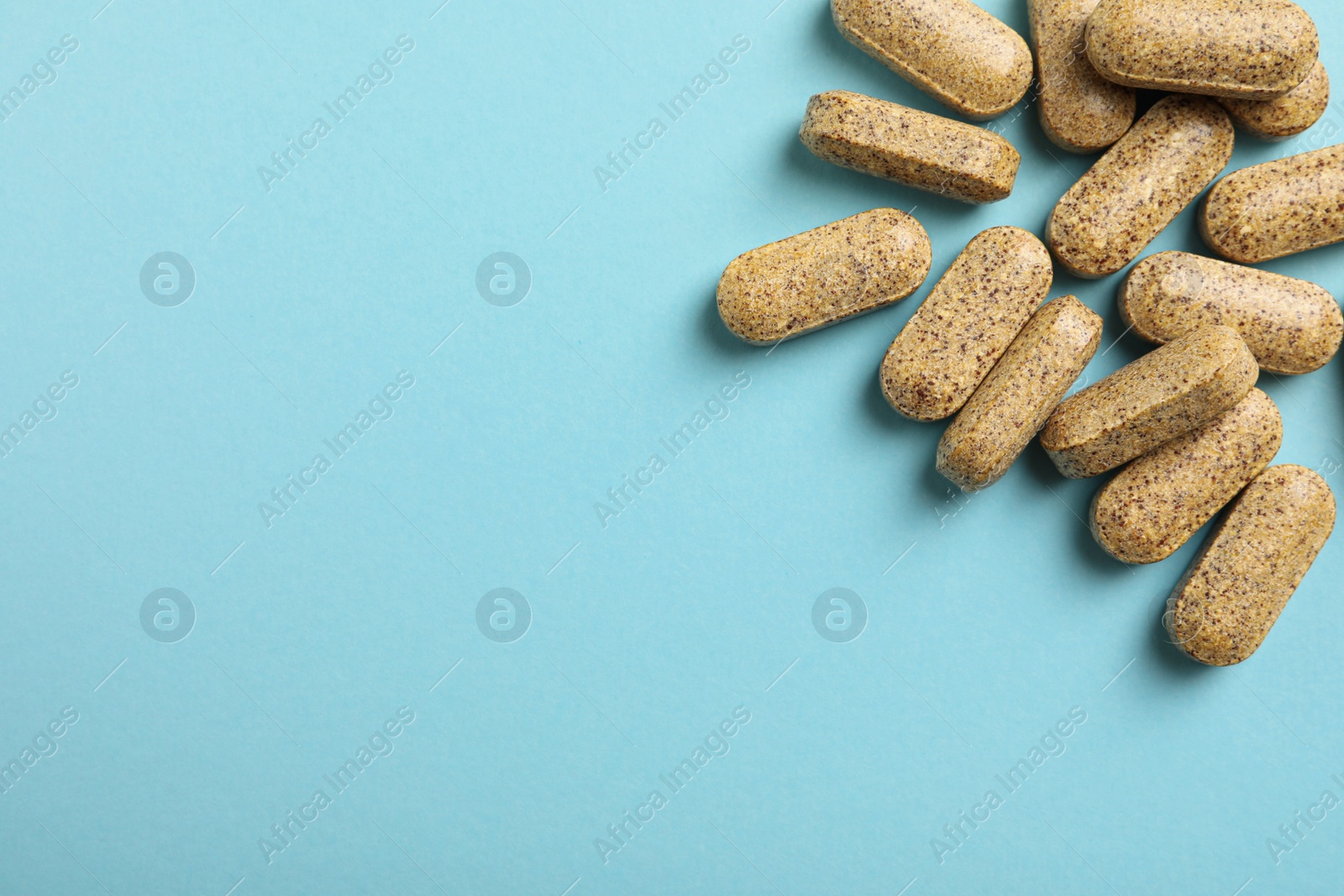 Photo of Dietary supplement pills on light blue background, flat lay. Space for text