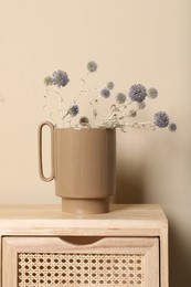 Stylish ceramic vase with wild flowers on wooden cabinet near beige wall