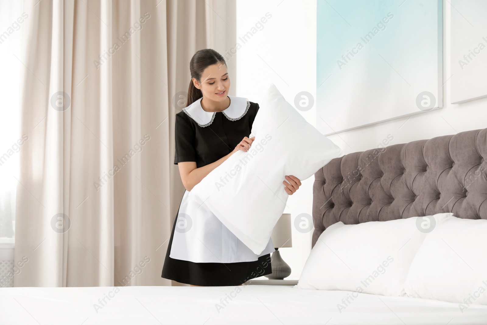 Photo of Young maid making bed in hotel room