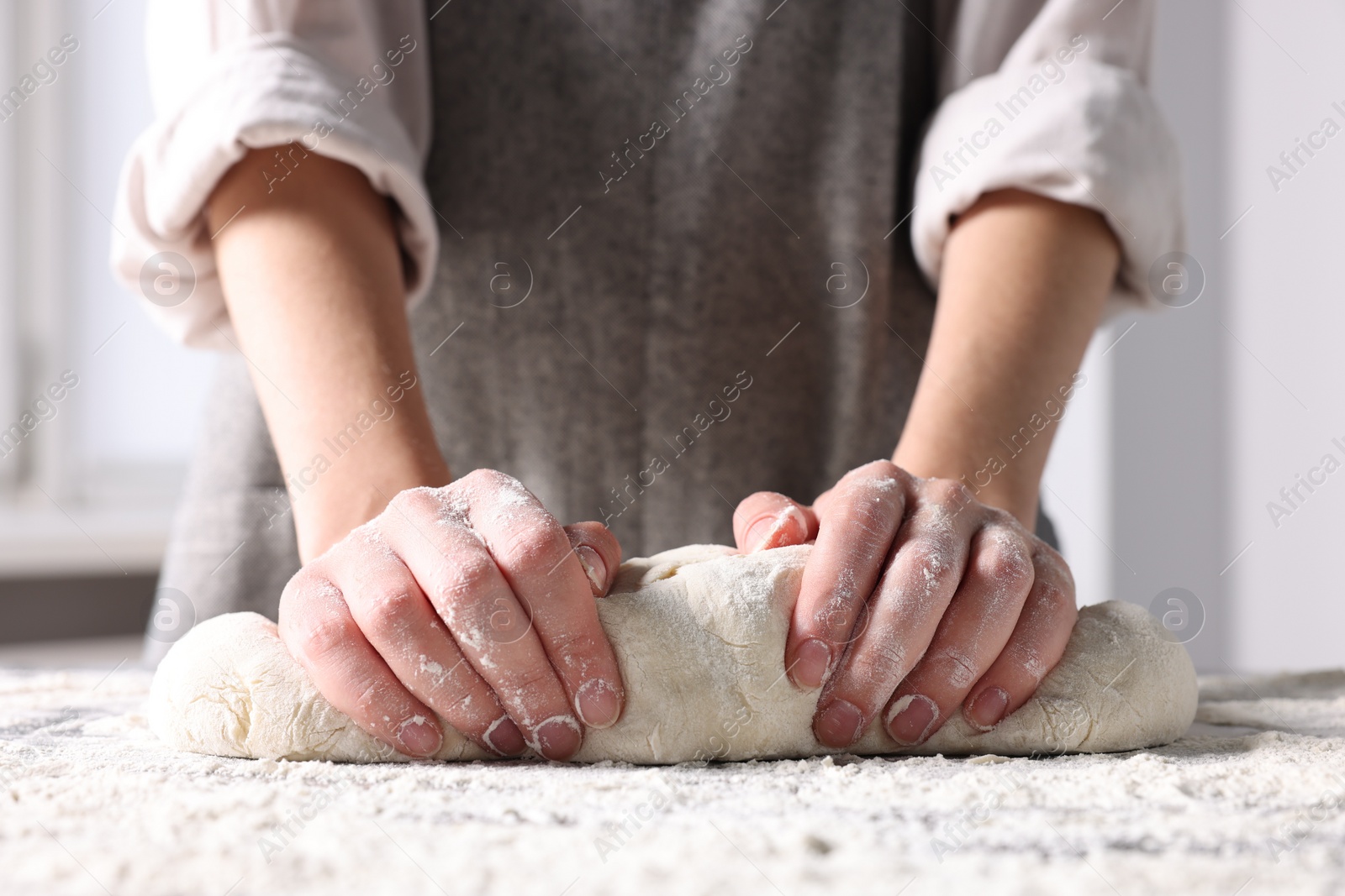 Photo of Woman kneading dough at table in kitchen, closeup