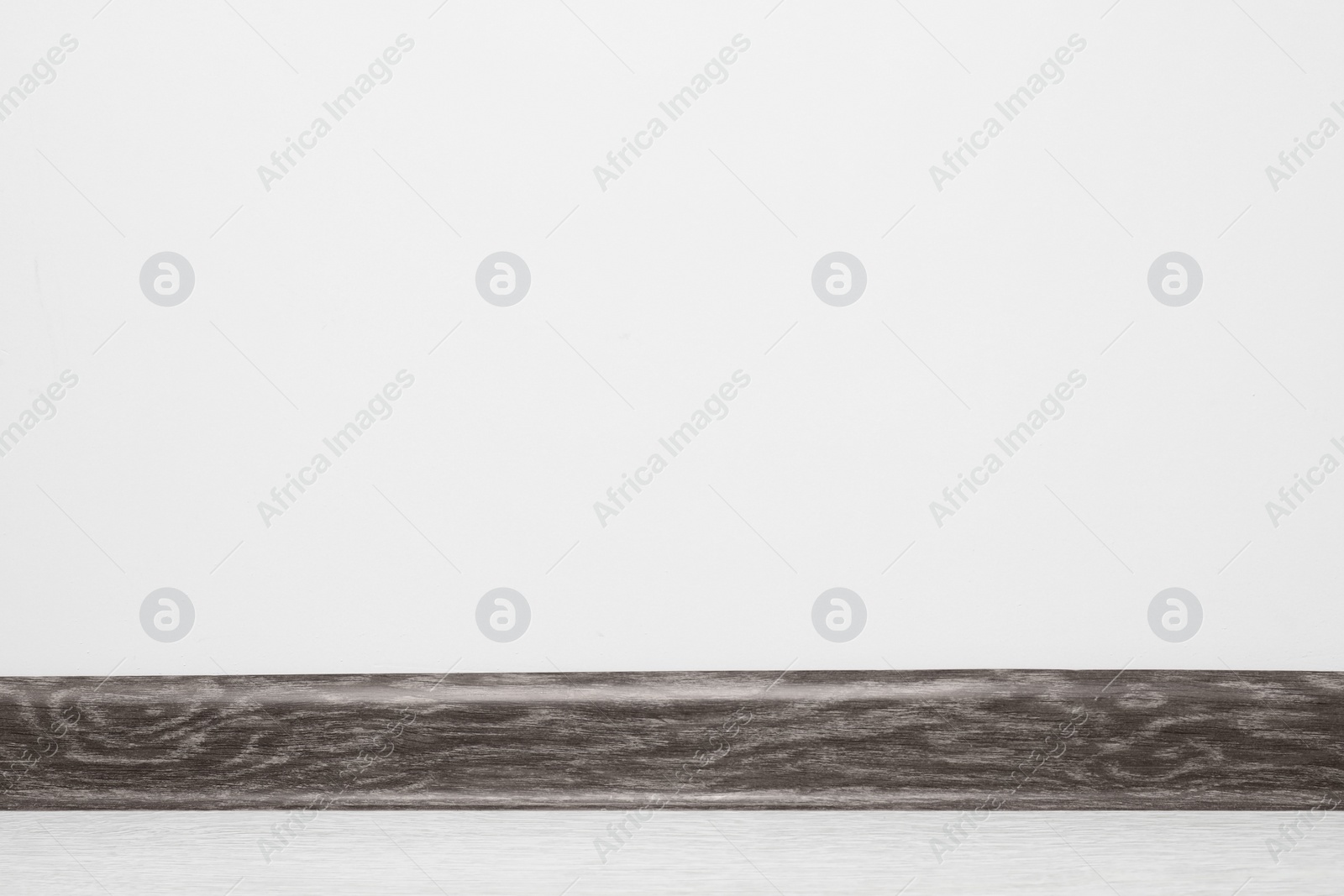 Photo of Black wooden plinth on laminated floor near white wall indoors