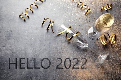 Image of Text Hello 2022, glasses and serpentine streamers on grey table, above view