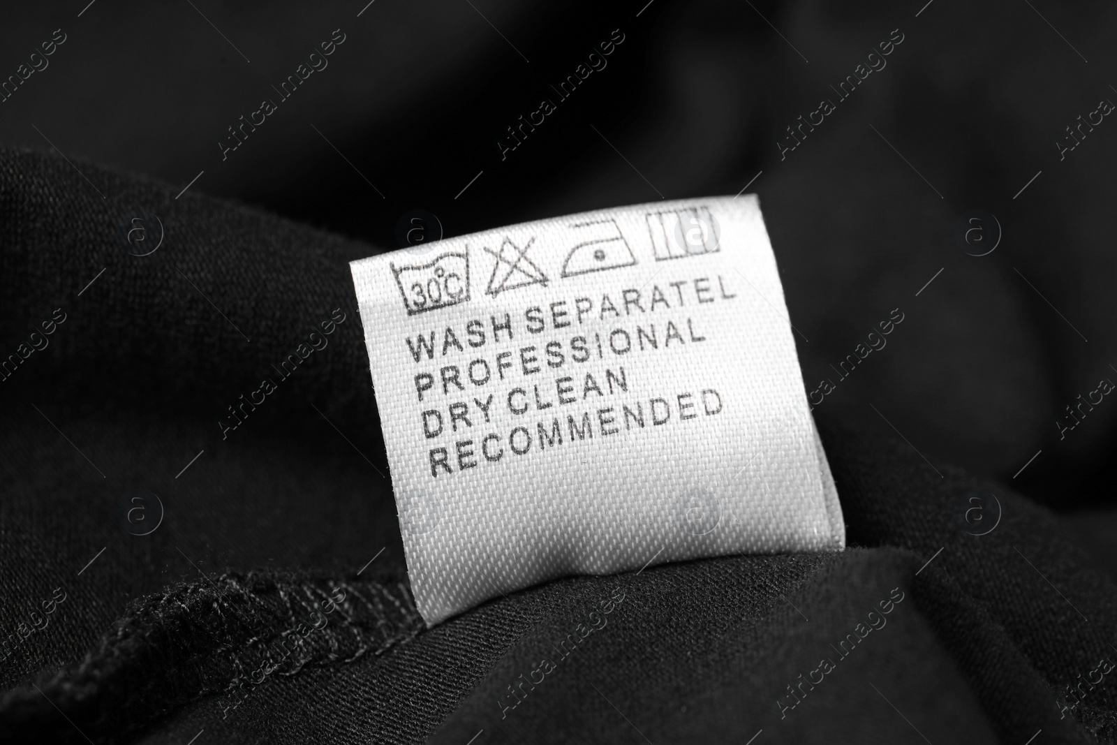 Photo of Clothing label with recommendations for care on black garment, closeup