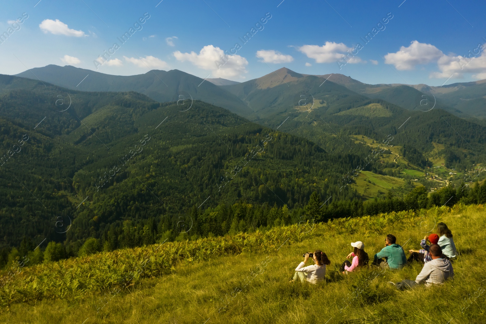 Image of Group of tourists sitting on hill in mountains